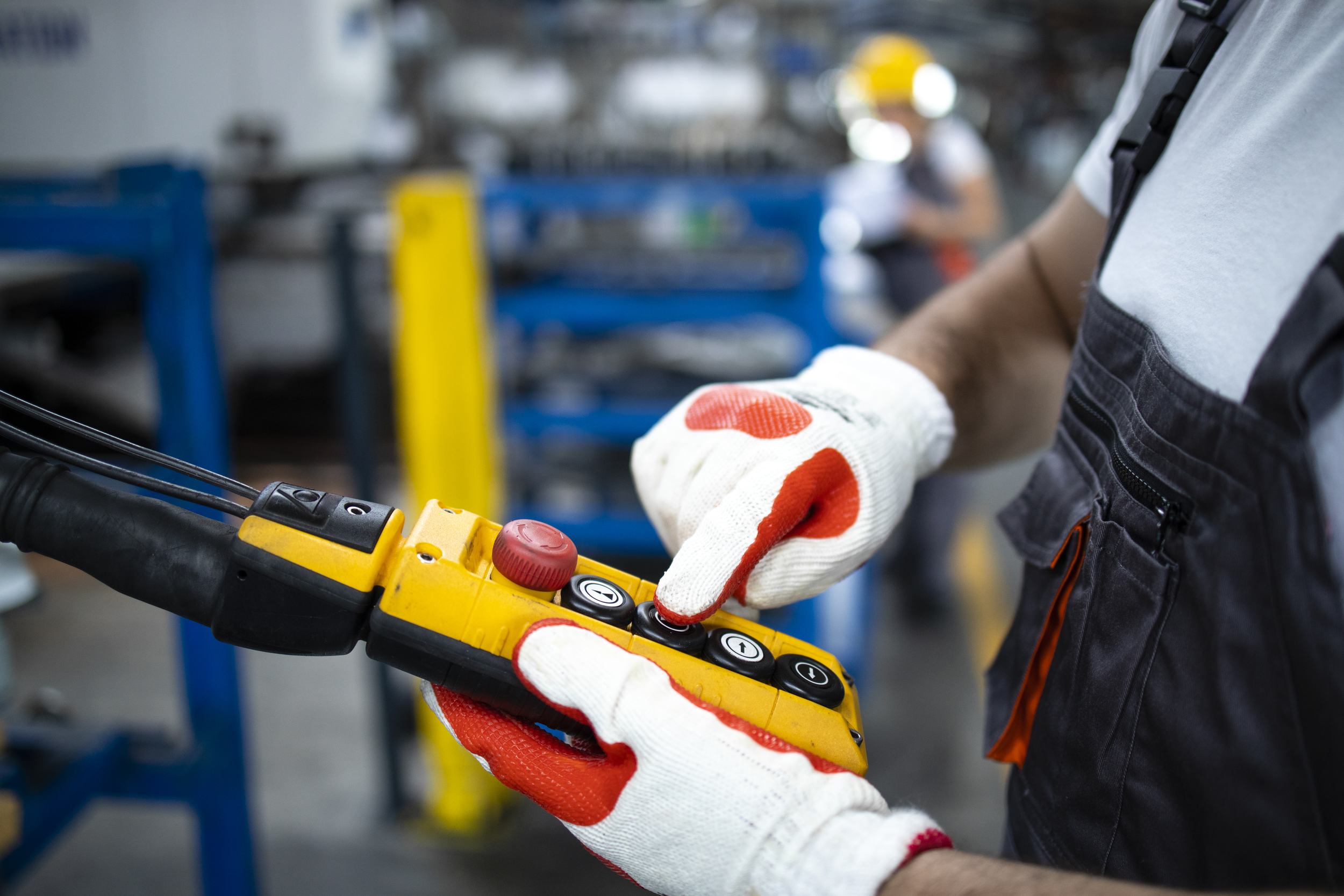 Close up view of factory worker operating industrial machine with push button joystick in production hall.